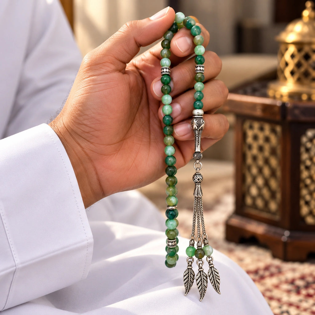 Hand holding Banded Green Agate tasbih with silver-tone detailing and three tassel chains with leaf charms.