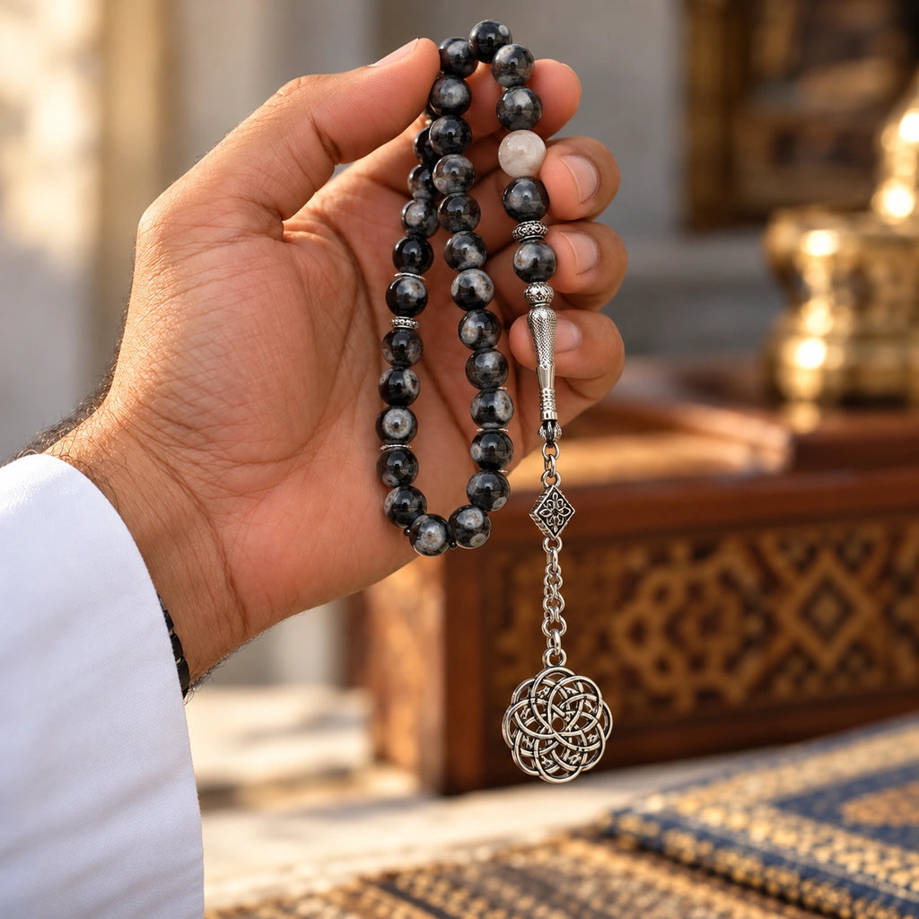 Hand holding Black Agate tasbih with mottled black beads and a silver-tone circular knot ornament.