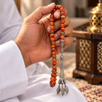 Hand holding striped orange Agate tasbih with silver-tone imame and three chains ending in wing-shaped charms.