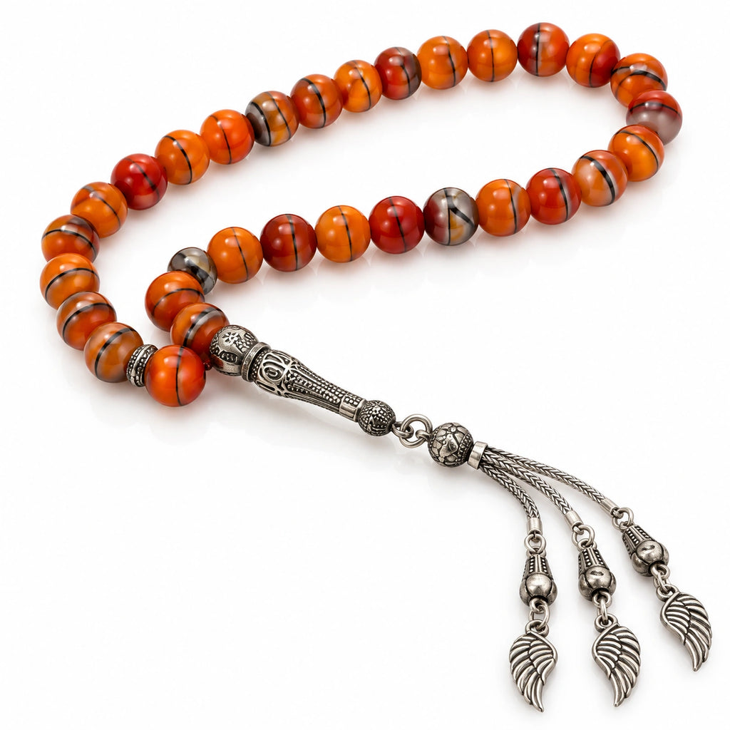 Striped orange Agate tasbih with silver-tone patterned imame and three wing-shaped tassel charms on white.