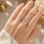 Hand wearing a ring with pink gemstones against a neutral background