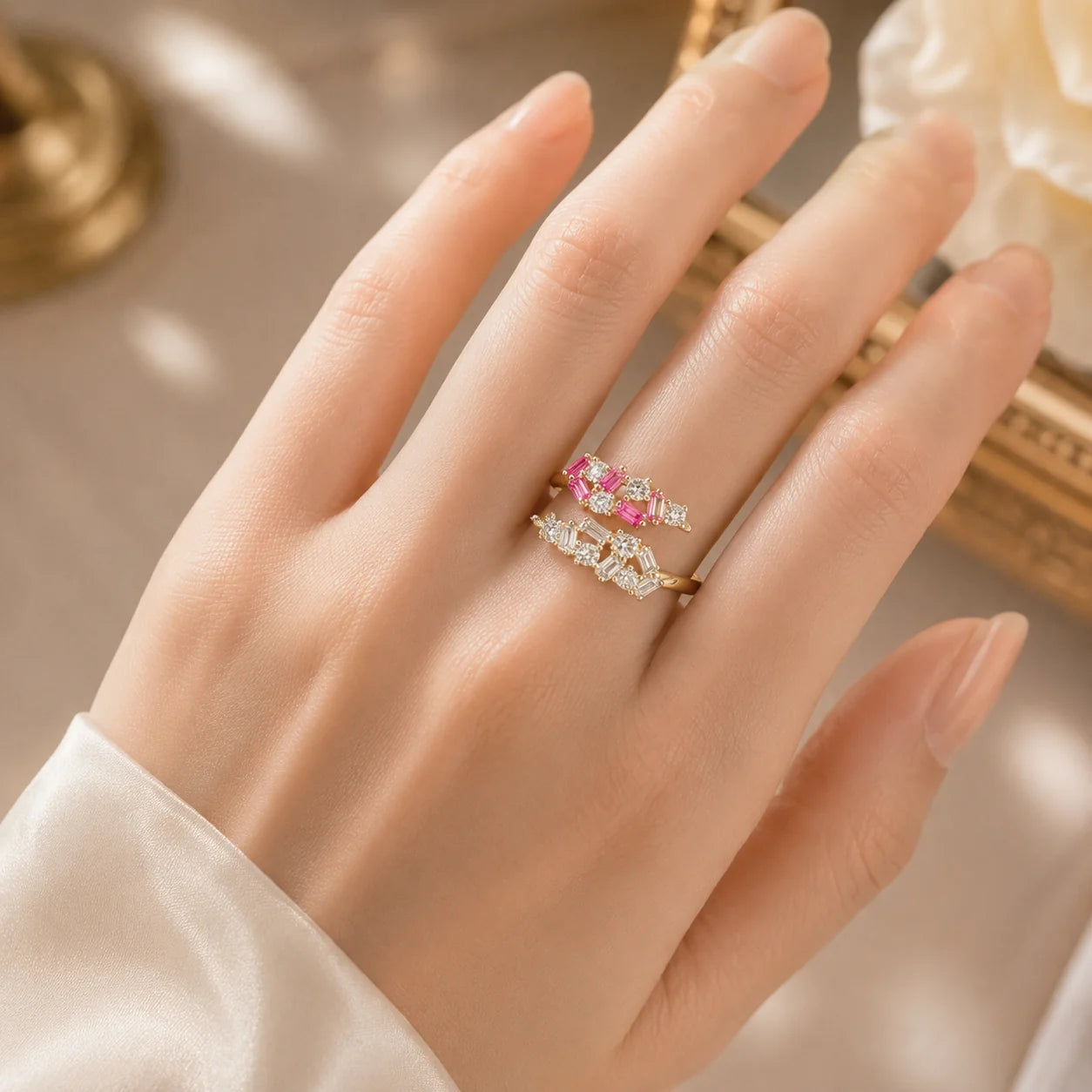 Hand wearing a ring with pink gemstones against a neutral background