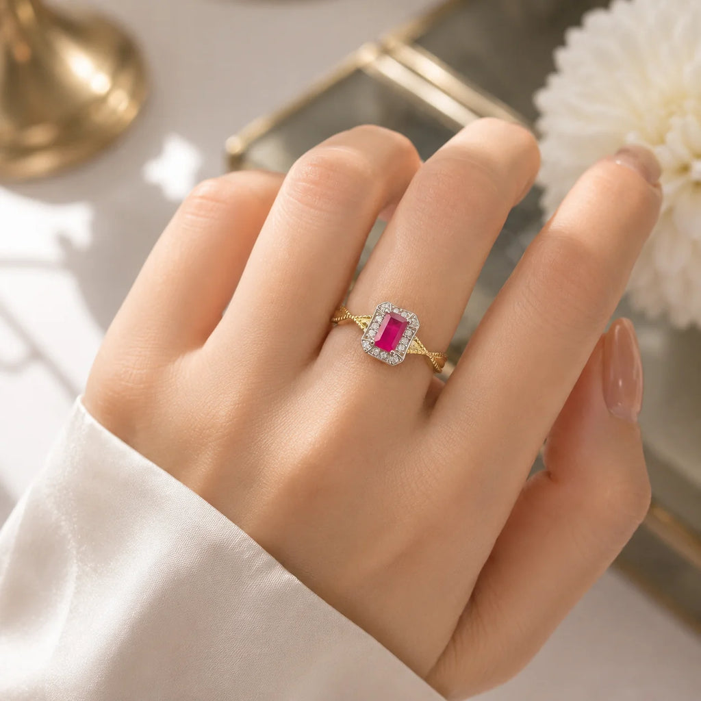 Gold ring with a pink gemstone on a hand against a neutral background