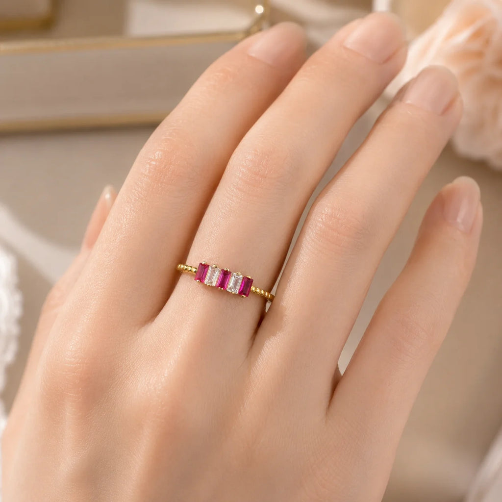 Gold ring with red gemstones on a hand against a neutral background
