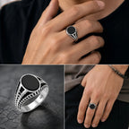 Silver ring with black stone on a hand against a dark background