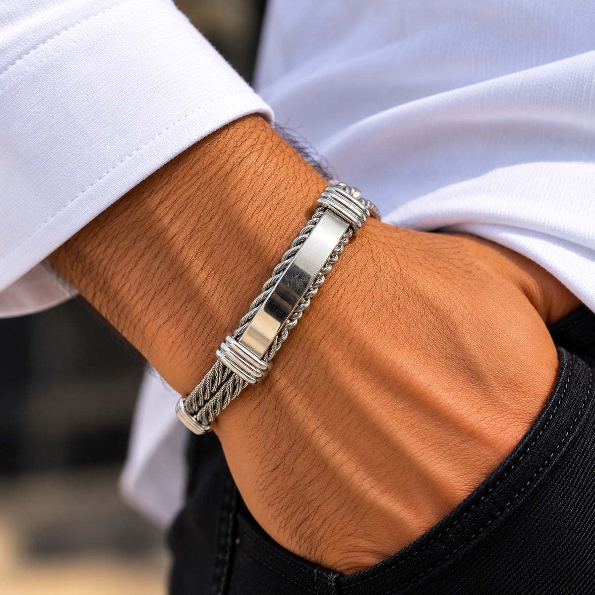 Men's silver cable cuff bracelet with a polished centre bar worn on a wrist beside a white cuff.
