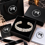 Silver chain-link cuff bracelet displayed in a black presentation box with branded bag, card, ribbon and cloth.