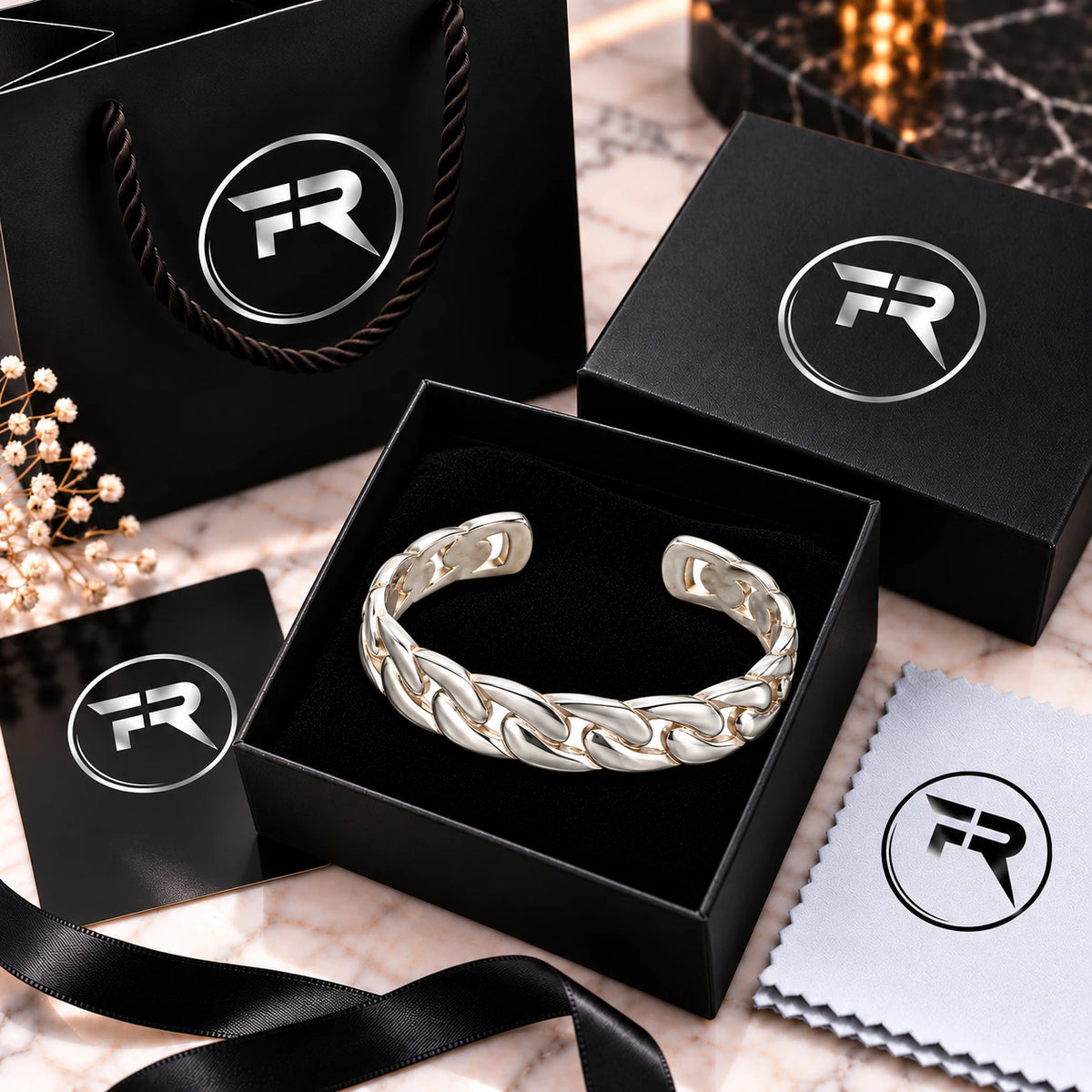 Silver chain-link cuff bracelet displayed in a black presentation box with branded bag, card, ribbon and cloth.
