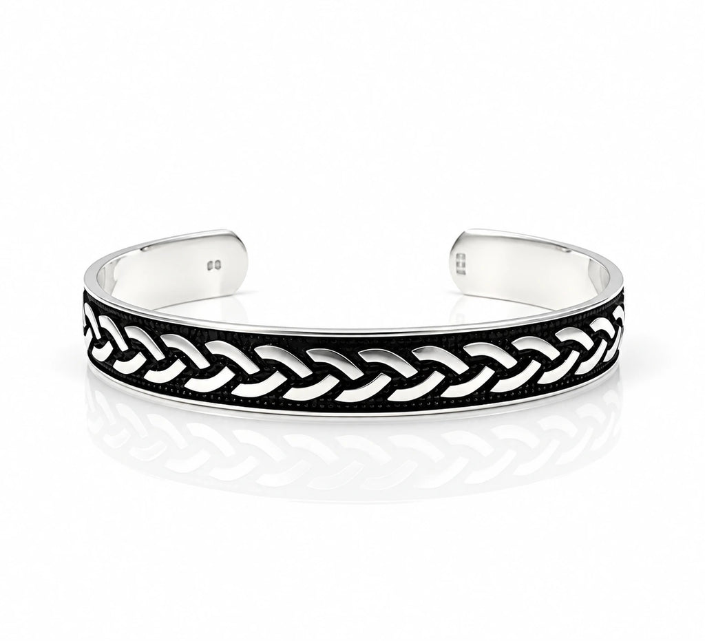 A silver-toned open cuff bracelet featuring a black enamel inlay with a raised braided chain pattern, photographed on a clean white background with a soft reflection.