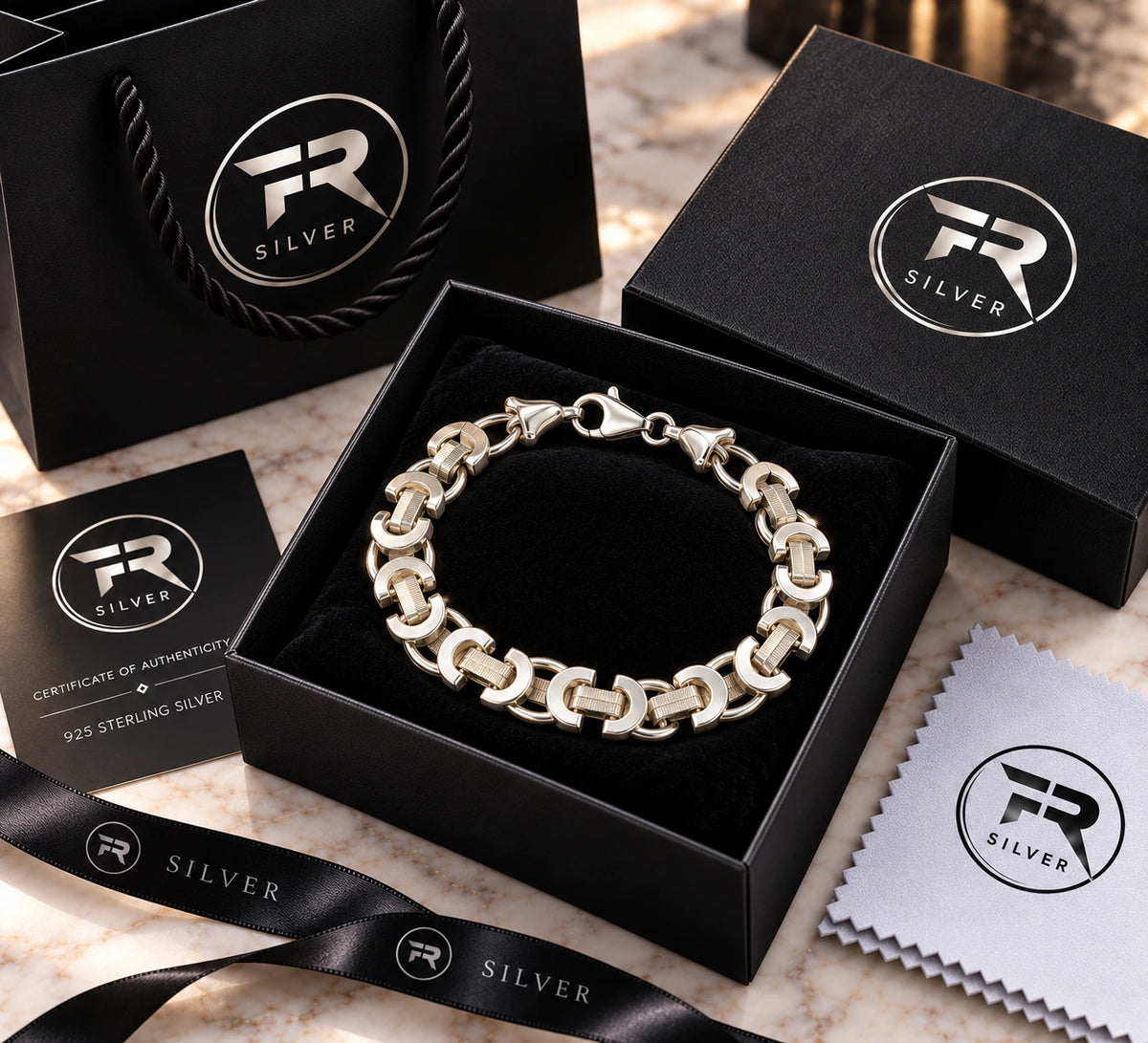 Silver crescent-link bracelet displayed in a black presentation box with branded bag, card, ribbon and cloth.