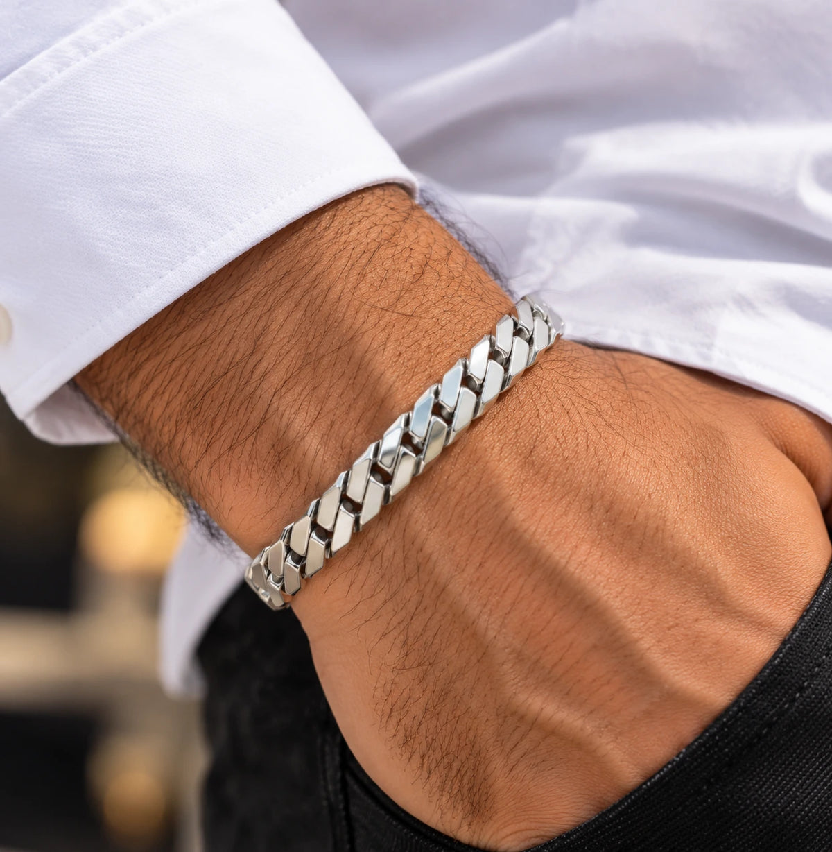 Men's polished silver Cuban-link bracelet worn on a wrist beside a white shirt cuff.
