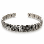 Men's silver open cuff bracelet with repeating diagonal scroll-patterned panels and dark antique-style recesses on white.