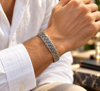 Men's antique-style engraved silver cuff bracelet worn on a wrist beside a white shirt cuff.