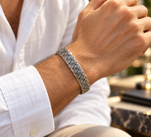 Men's antique-style engraved silver cuff bracelet worn on a wrist beside a white shirt cuff.