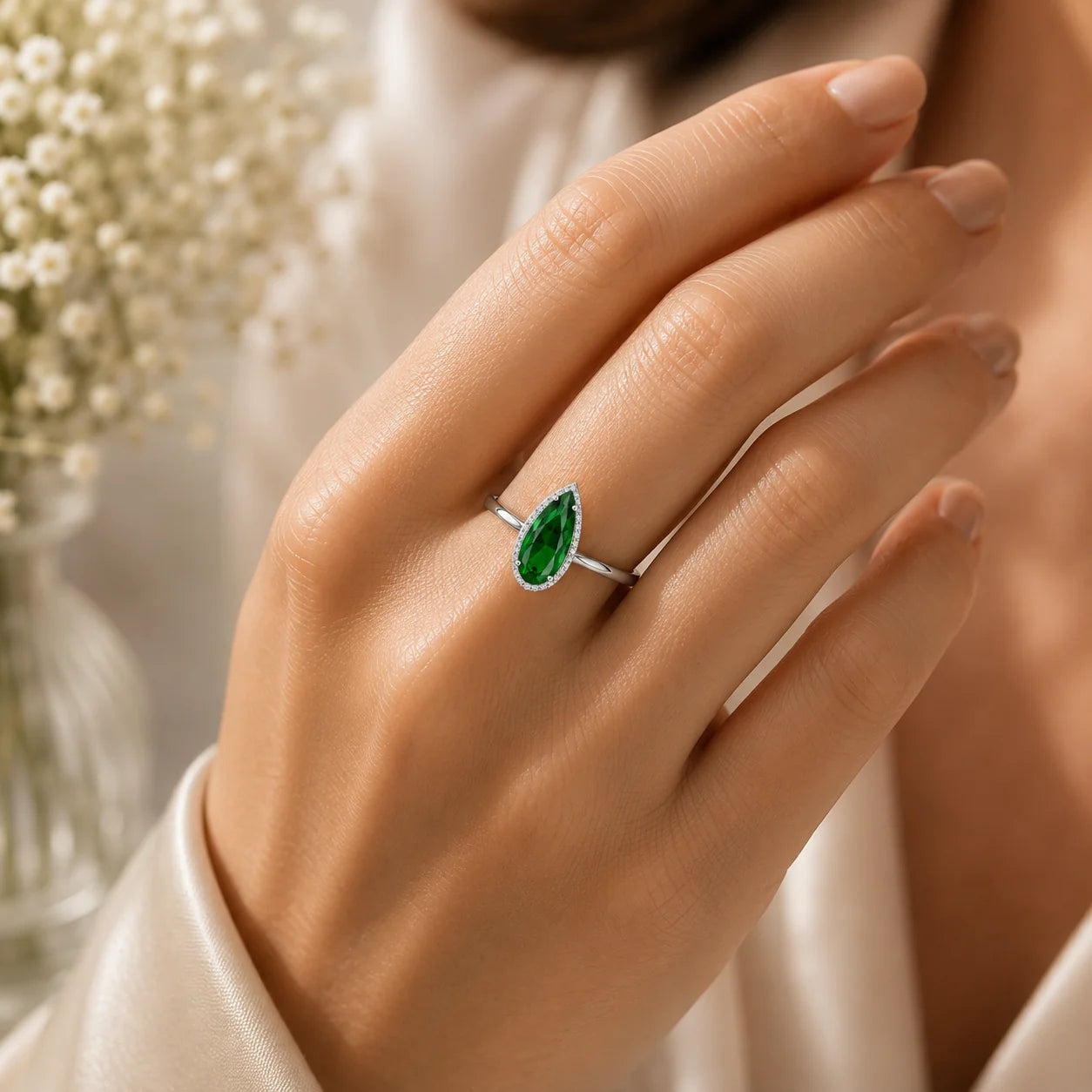 Hand wearing a ring with a green gemstone against a blurred floral background