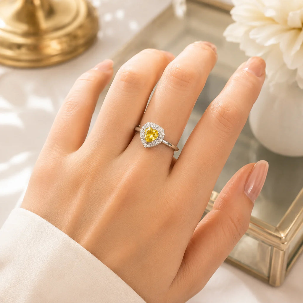 Hand wearing a silver ring with a yellow gemstone on a reflective surface.