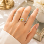 Hand wearing a silver ring with a yellow gemstone on a reflective surface.